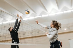 Two athletes engaged in a thrilling volleyball match indoors, showcasing competitive spirit and energy.