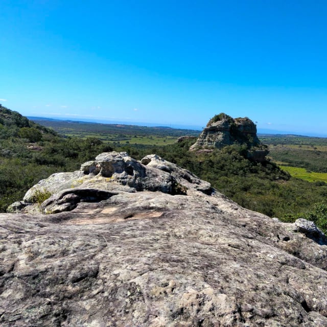 Rochas de arenito em primeiro plano com vista ampla de vales e formações rochosas sob céu azul