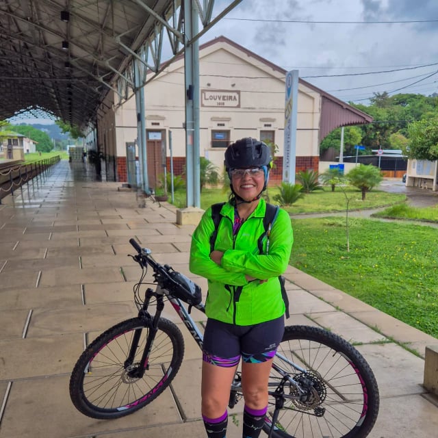 Ciclista de jaqueta verde e capacete ao lado da bicicleta, em frente à antiga estação ferroviária de Louveira