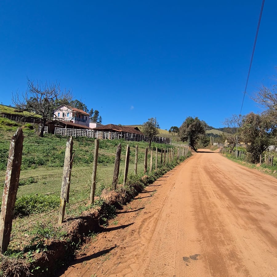 Estrada de terra com cerca de madeira, casas e pastagem sob céu azul