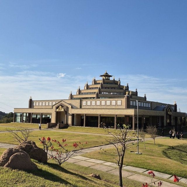 Fachada do Templo Budista Kadampa com jardins e gramados sob céu azul