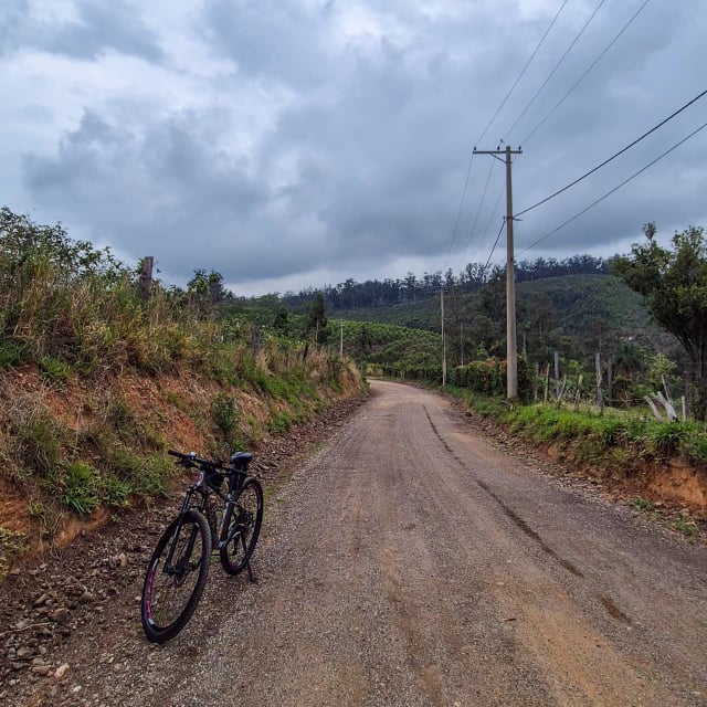 Bicicleta apoiada na beira de uma estrada de cascalho, com morros e vinhedos ao fundo