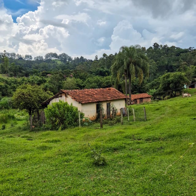 Casa antiga de telhado vermelho em meio a um campo verde e árvores no interior paulista