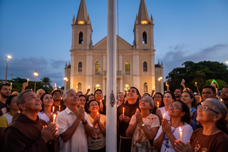 Uma fotografia vibrante e emocional capturada ao final da tarde em Canindé. Centenas de romeiros estão reunidos na praça em frente à Basílica. O foco está no momento do Hasteamento das Bandeiras. Uma luz quente de pôr do sol ilumina a cena, criando uma atmosfera de devoção e comunidade.