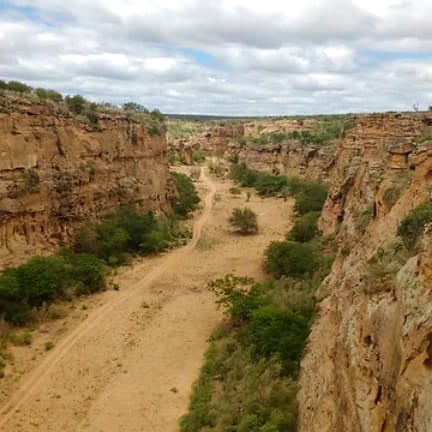 Vale estreito de arenito com trilha de terra batida entre paredões rochosos e vegetação de Caatinga