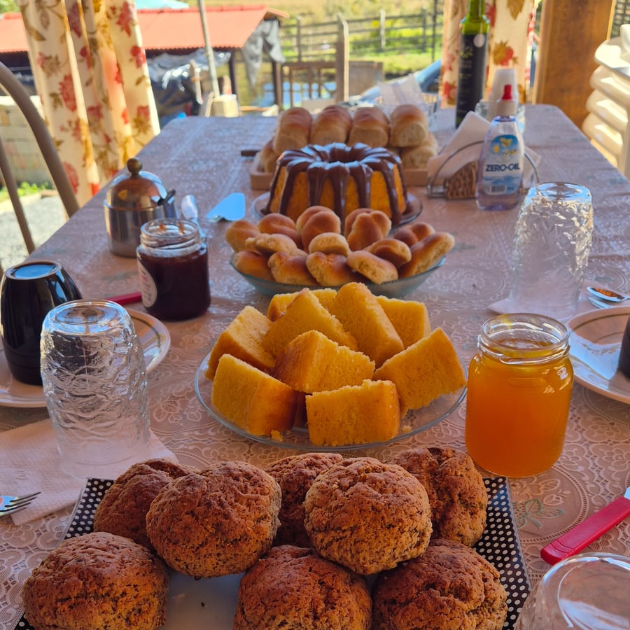 Mesa de café da manhã com pães, bolo com cobertura de chocolate, broas, geleia e mel