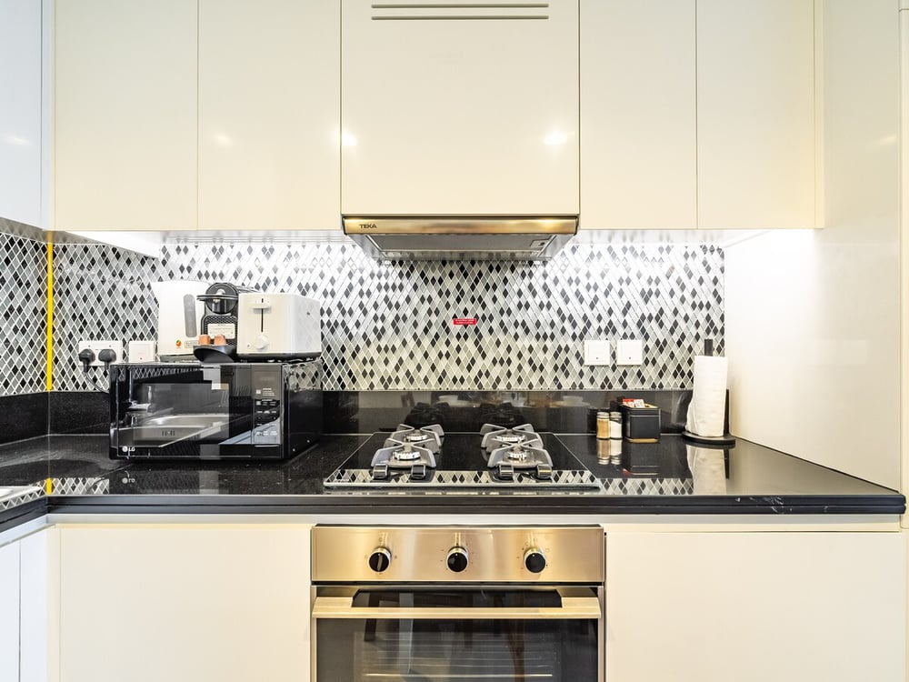 Kitchen with gas hob, oven, white cabinets and mosaic backsplash