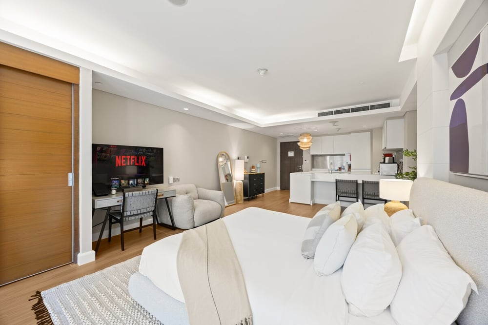 Studio bedroom area with king bed, TV and kitchen in background