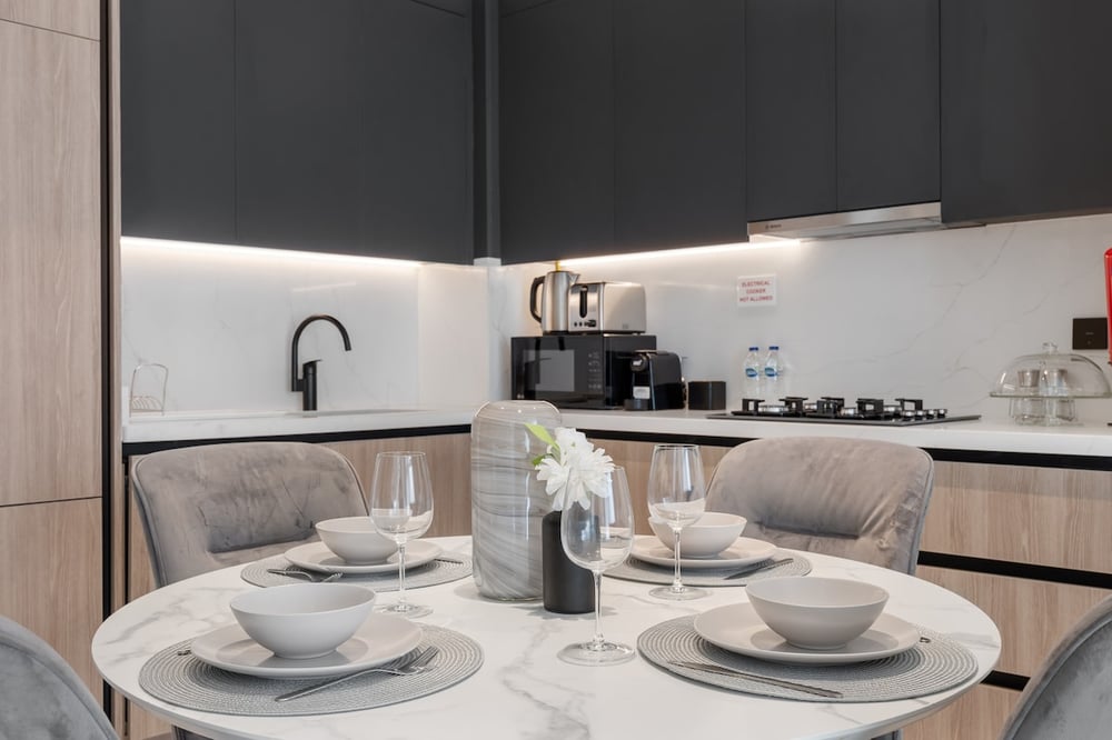 Dining table with place settings, wine glasses and kitchen behind