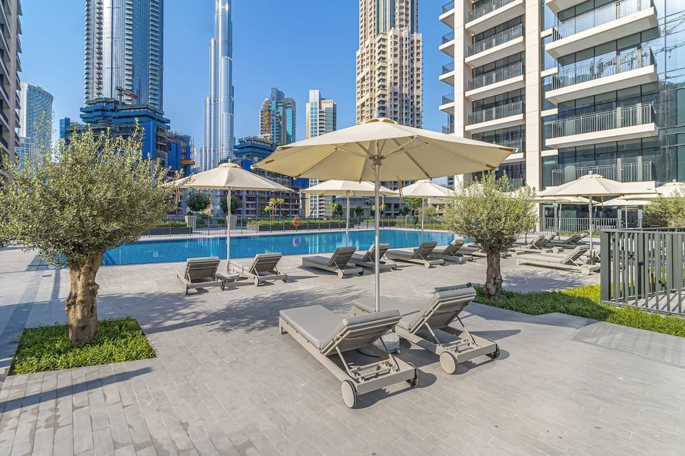 Outdoor pool area with parasols and sun loungers among skyscrapers