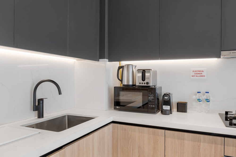 Kitchen counter with sink, kettle, microwave and dark upper cabinets