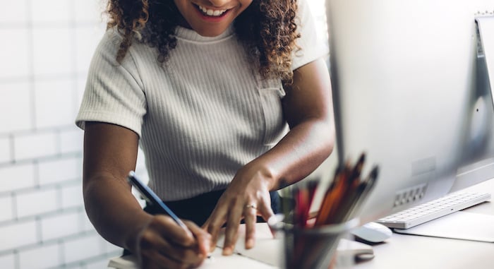 Person writing a resume at a desk beside a computer.