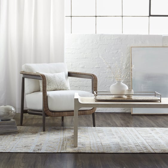 A modern thick cushioned chair faces a modern white coffee table. They sit on a white patterned rug.