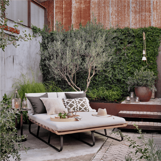 Double sized chaise styled with pillows on a patio surrounded by plants.