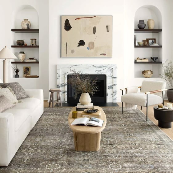 Living room decorated in an organic modern style with netural furniture, wooden coffee table, and abstract art hung above a marble fireplace mantle.