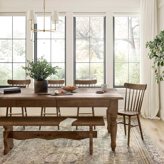 Modern farmhouse style dining room featuring a round wooden table surrounded by four black dining chairs. A neutral rug anchors the space, and ceramic vases adorn the table, blending rustic charm with contemporary design.