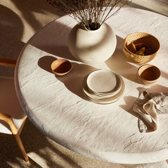 White textured concrete table adorned with beautifully arranged earthenware dinnerware, complemented by a ceramic vase holding elegant branches. A harmonious blend of textures and natural elements, creating a serene and inviting tabletop setting.
