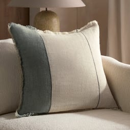 Neutral accent pillow with wide contrasting stripe and frayed edges, styled on a textured cream sofa for a modern layered look.