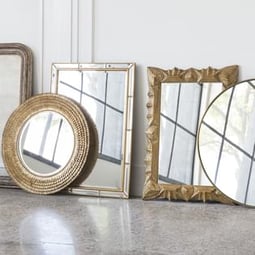 Several wall mirrors - some round, some rectangular - lay against the base of a white wall.