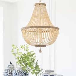 A golden beaded chandelier hangs above a green plant and blue china vases.