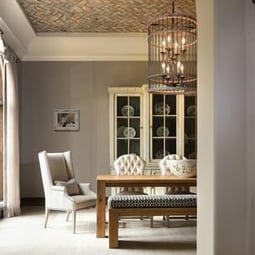 A warmly lit room with detailed furniture and a large hutch. A large caged chandelier hangs above the room from a brick ceiling.