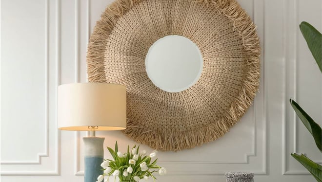 Round rattan mirror from Made Goods hanging on white paneled wall