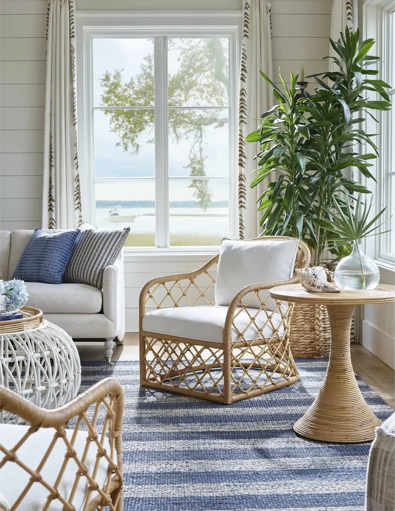 Coastal living room featuring a cane arm chair next to a rattan side table on top of a blue striped rug.