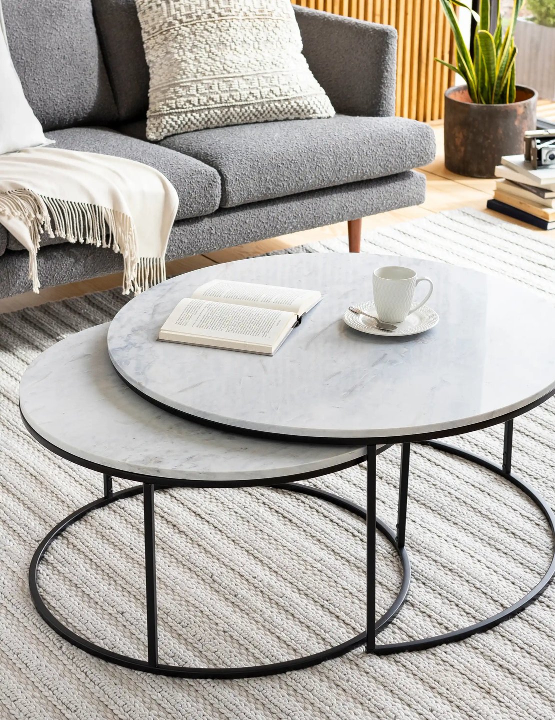 Two nesting round marble coffee tables on stop of a natural rug.