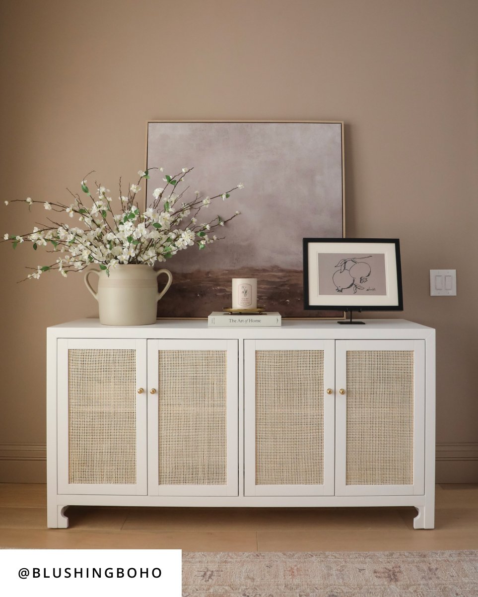 Design by @blushingboho, A white sideboard with a beautiful picture displayed on it.