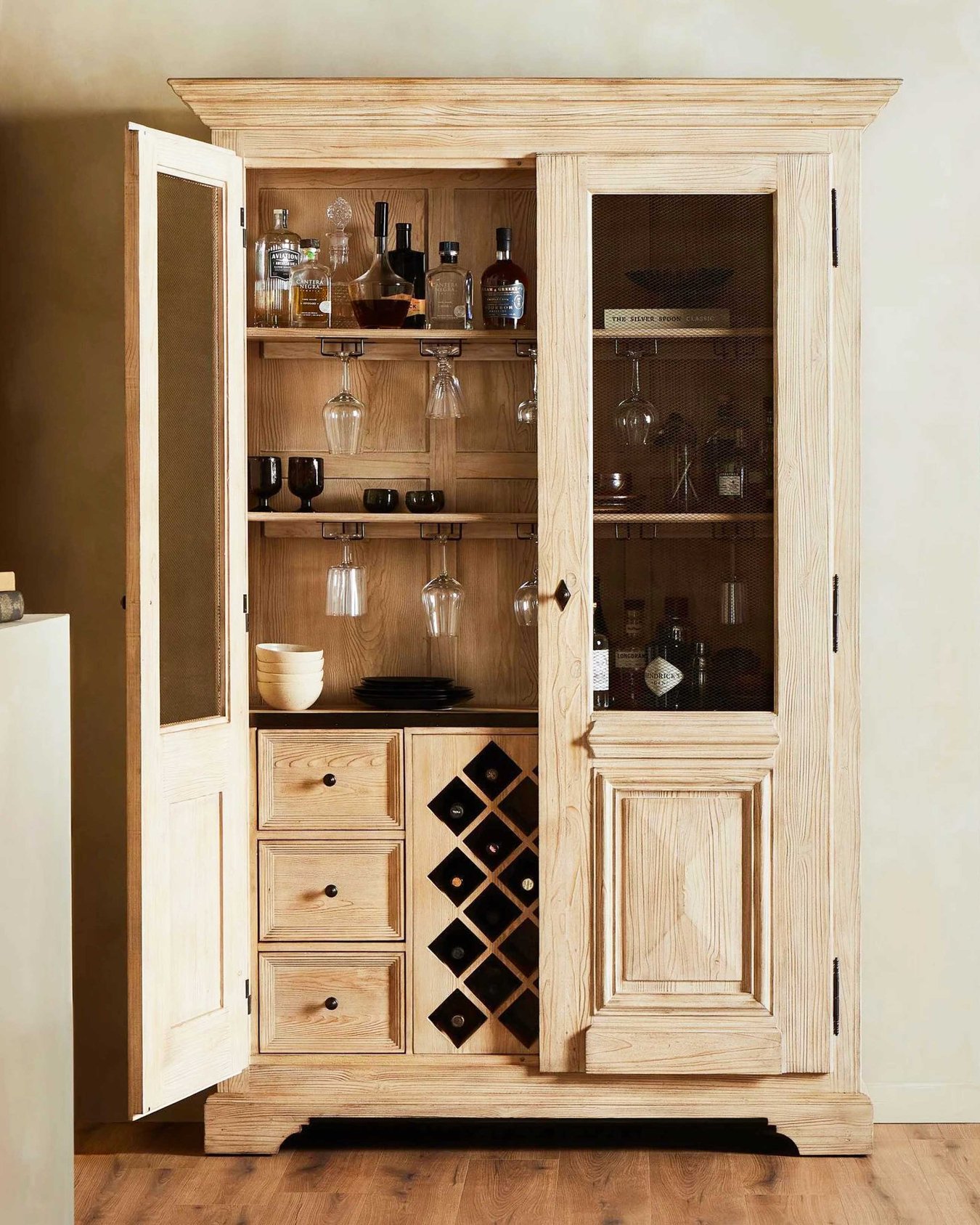 A light wood traditional cabinet with drinking glasses and bottles.