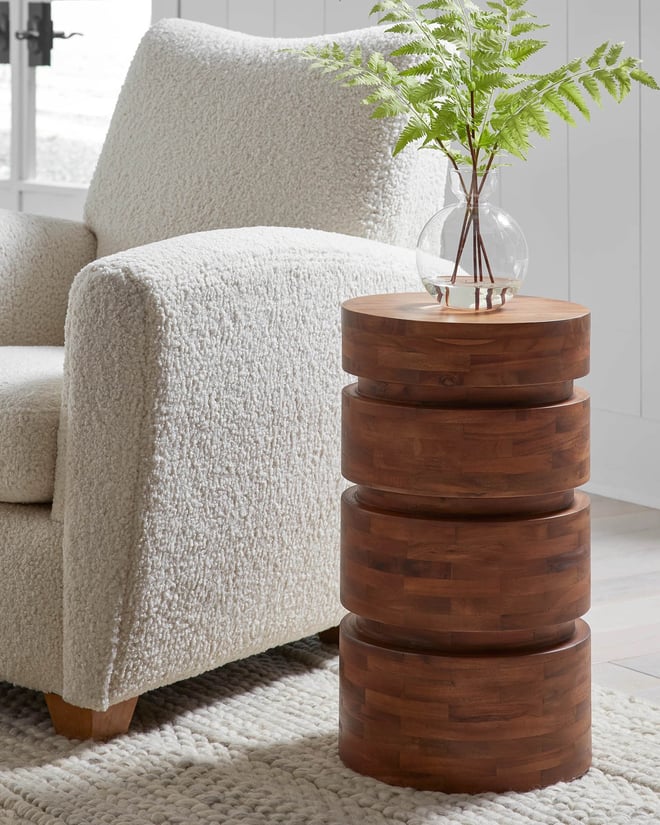 Cylinder shaped wooden side table with vase of ferns on top.