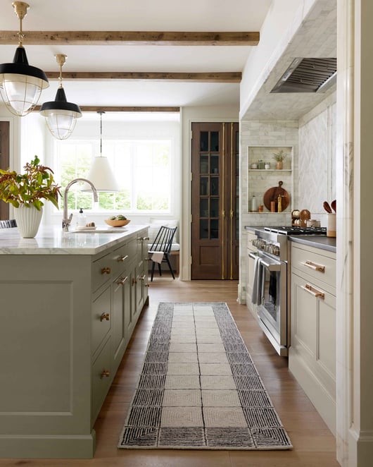 A kitchen with cream colored cabinets and a wooden island. There is a vintage inspired runner rug.