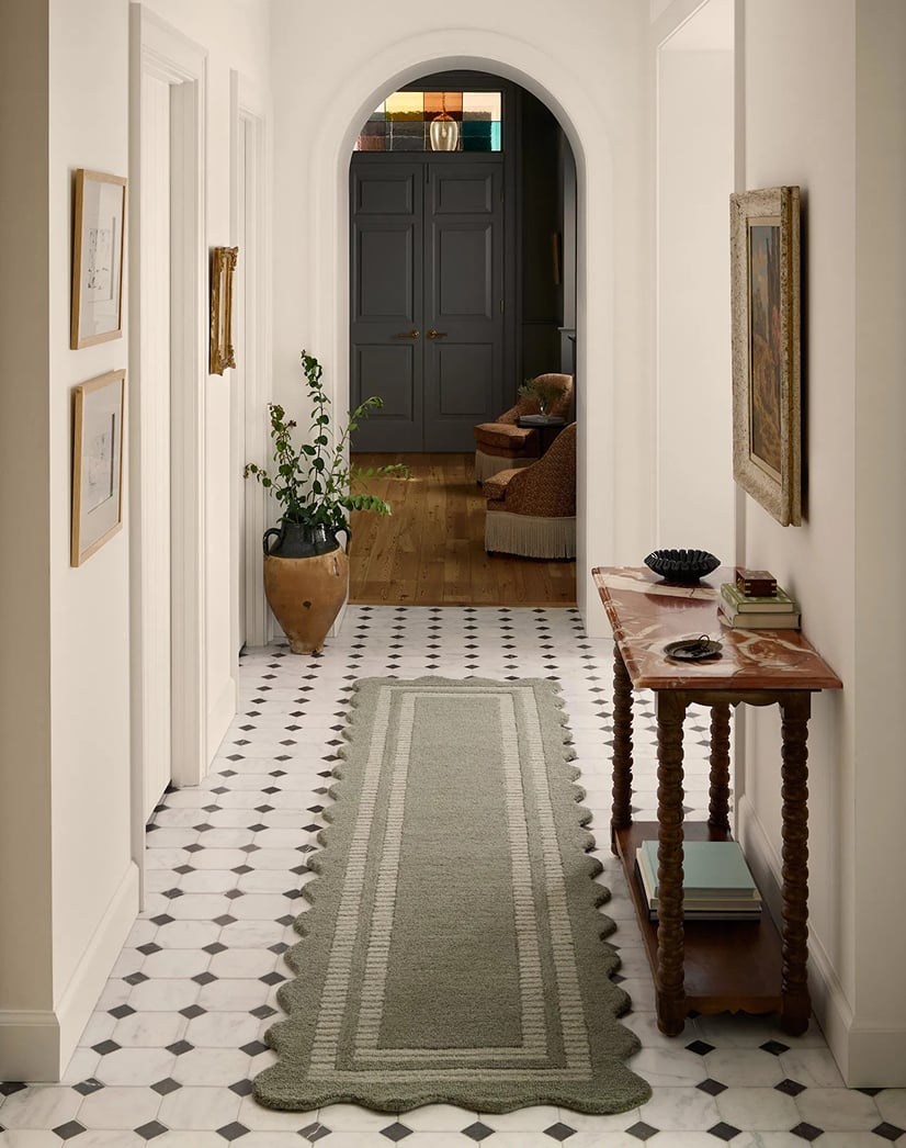 Elegant hallway styled with a scalloped-edge green runner rug, adding charm and softness to a classic black and white tiled floor on a premium rug website.