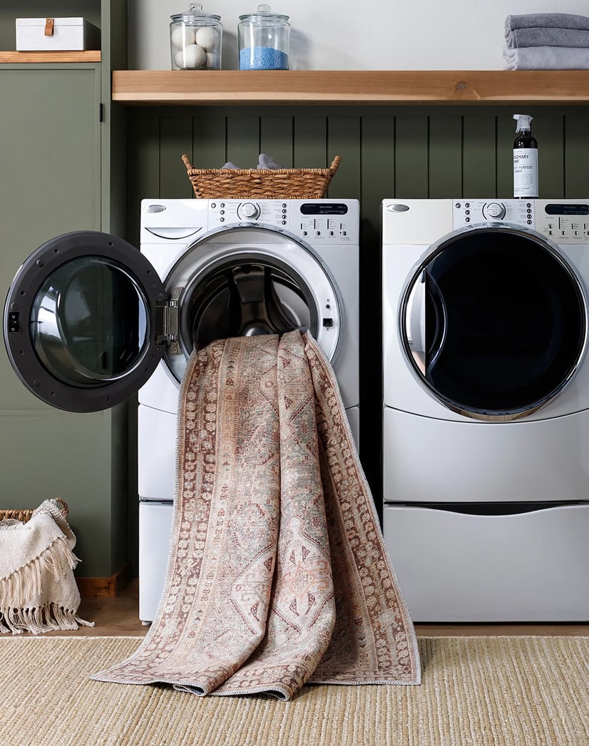 Vintage-style washable area rug being loaded into a front-loading washing machine, highlighting easy-care convenience for modern rug shoppers.