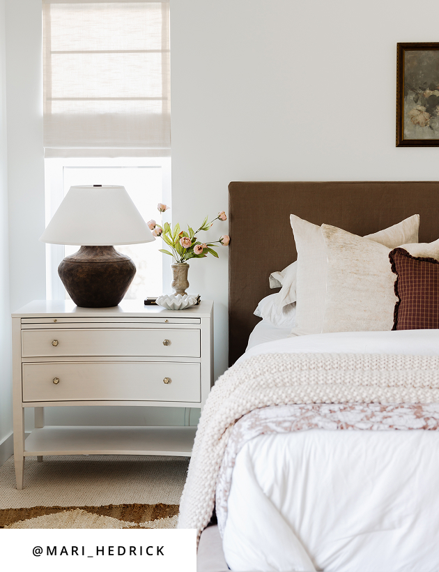 Neutral bedroom styled with upholstered bed, wood table lamp, and classic nightstand accents