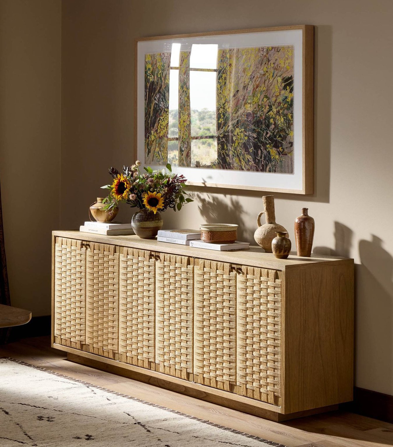 Woven wood sideboard styled with framed art, pottery, and warm neutral decor in a sunlit room