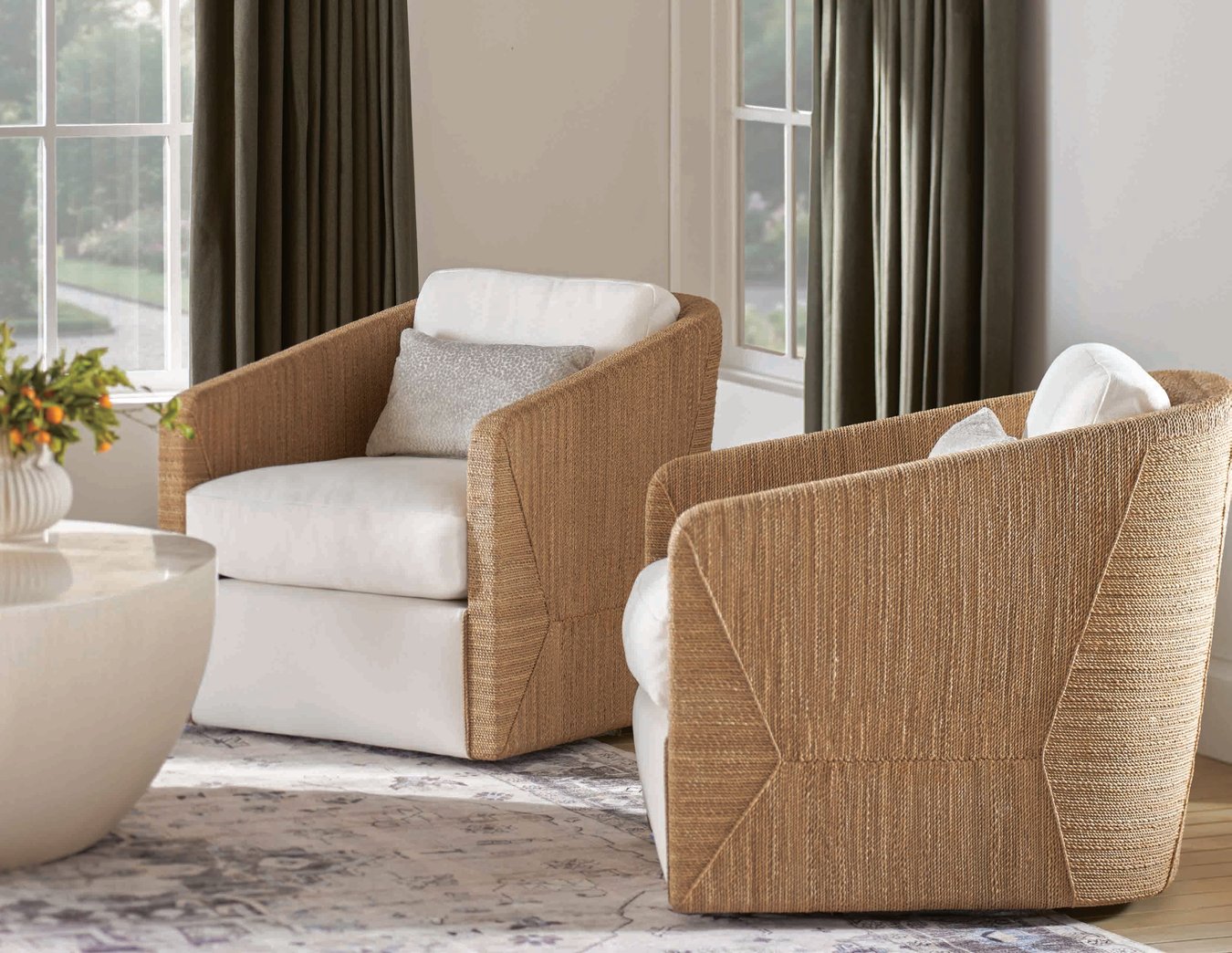 Woven accent chairs with white cushions in neutral living room with soft rug and drapery.