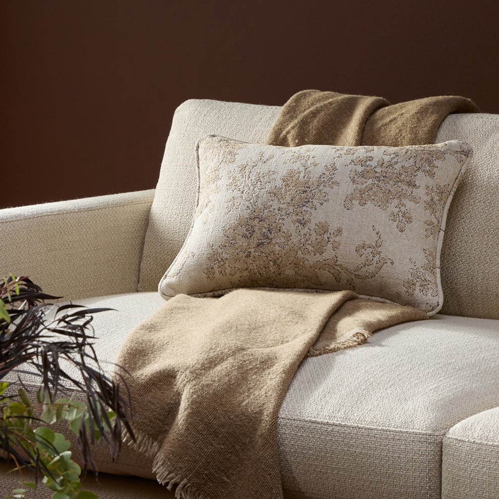 Close-up of neutral sofa with textured pillow and throw in warm, earthy tones.