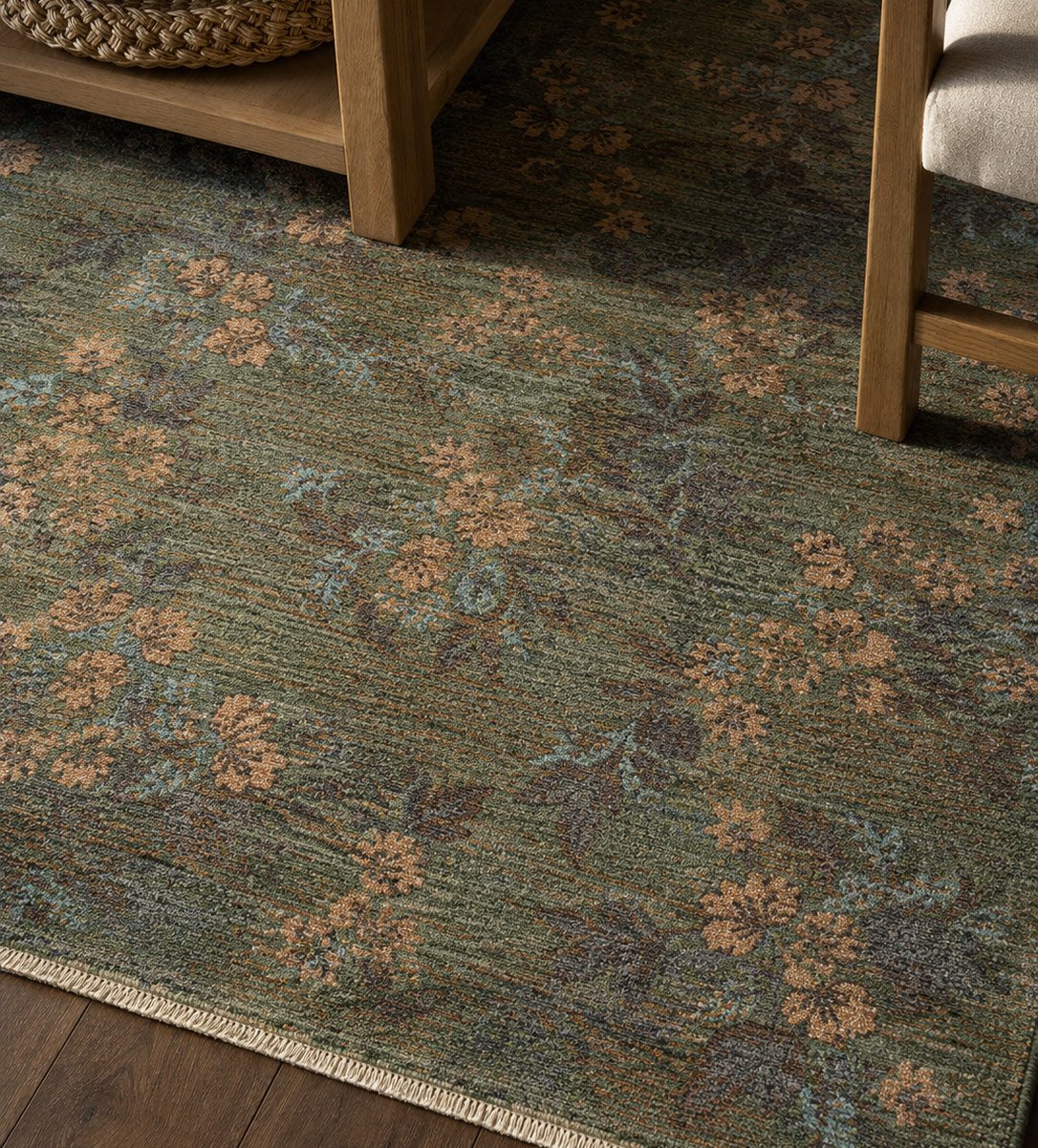 Close-up of vintage-style floral rug in green and rust tones with wood furniture.