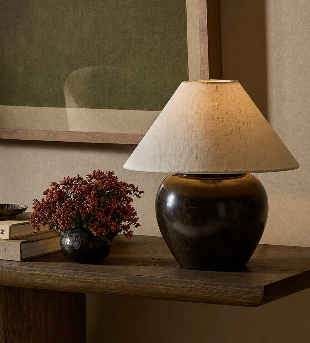 Wood console table with ceramic lamp, books, and floral arrangement in warm neutral setting.