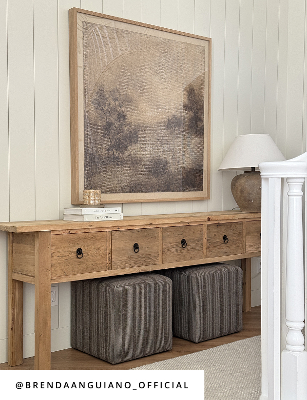 Entryway with rustic wood console table, striped ottomans, neutral artwork, and table lamp