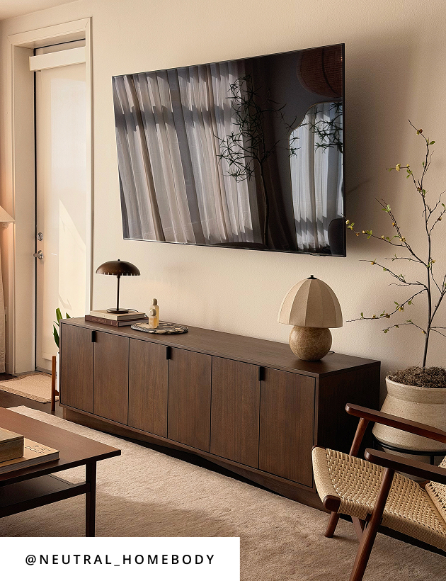Warm modern living room with wood media console, woven accent chair, and sculptural lamps