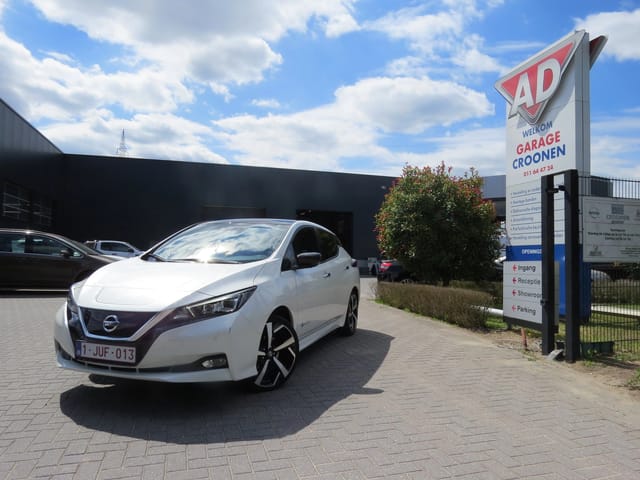 Witte Nissan-auto geparkeerd voor een gebouw en een bord van Garage Croonen met diensten en richtingen