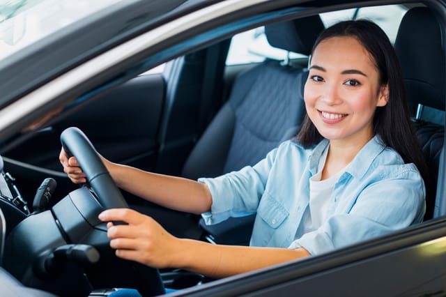 Jonge vrouw die achter het stuur van een auto zit en glimlacht