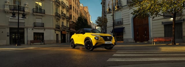 Gele Nissan Juke auto geparkeerd op een kruispunt in een Europese stadsstraat
