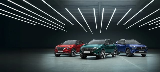 Drie moderne Nissan-auto's in verschillende kleuren (rood, groen, blauw) tentoongesteld in een donkere ruime showroom met stijlvolle lineaire plafondverlichting.