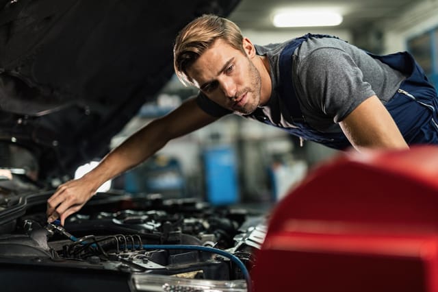 Een jonge monteur die een automotor in een werkplaats inspecteert en repareert