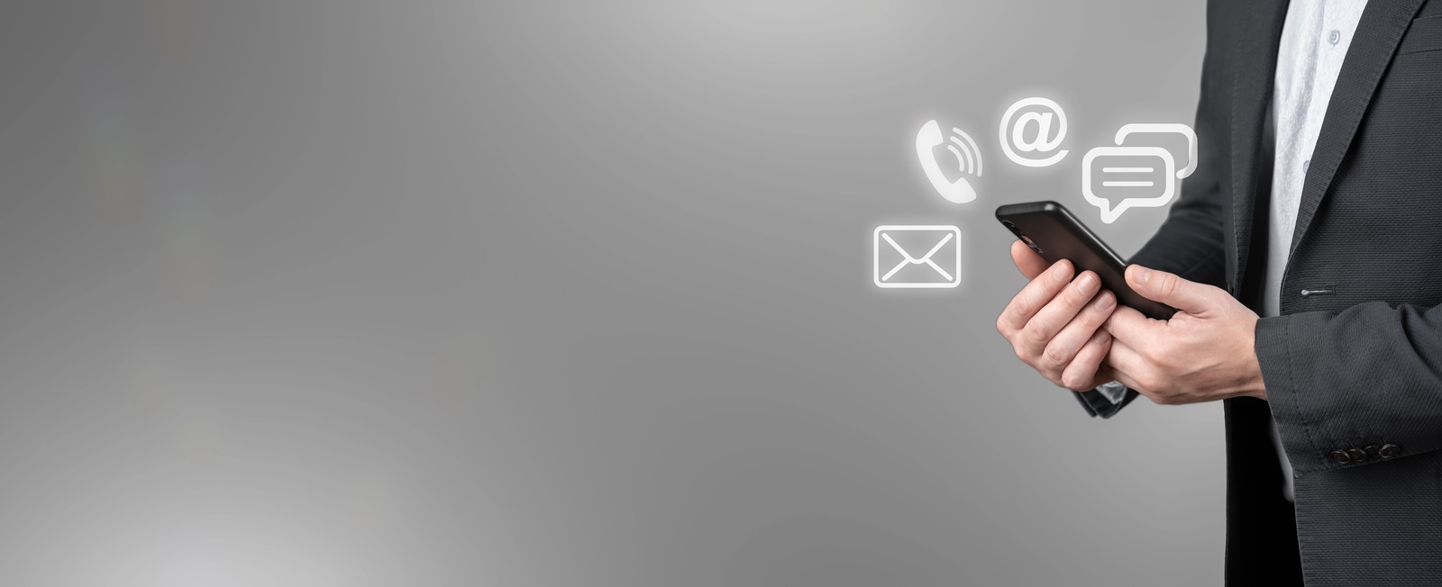 Une personne en costume sombre tenant un smartphone avec des icônes de communication lumineuses comme téléphone, e-mail et messages flottant sur un fond gris.