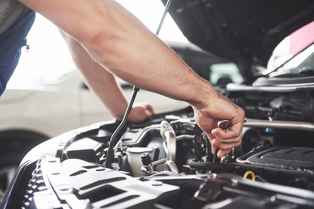Close-up van iemands arm die met een sleutel aan de motor van een auto werkt met de motorkap open.
