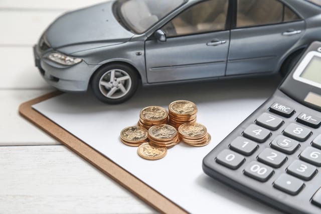Zicht van dichtbij op een modelauto, stapels munten en een rekenmachine op een klembord